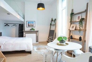 Une chambre moderne avec un lit, une table de salle à manger ronde entourée de chaises, une cheminée et une grande fenêtre.