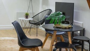 Ein modernes Loft-Apartment mit Essbereich, ausgestattet mit schwarzen Stühlen mit Holzbeinen, einem runden Tisch und einer großen Pflanze. Ein Flachbildfernseher ist an der Wand angebracht und ein Oberlicht sorgt für natürliches Licht.