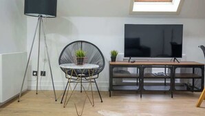 Ein modernes Wohnzimmer mit einer schwarzen Stehlampe, einem runden schwarzen Sessel mit einem weißen Tisch, einem Fernseher auf einem Holzständer und einem Oberlicht.