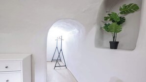 Un couloir étroit, avec une commode blanche sur la gauche, un trépied noir au centre et une plante en pot sur la droite.