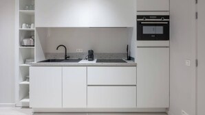 Une cuisine compacte avec des meubles blancs, un four encastré et une machine à café.