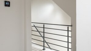 Un couloir avec un mur blanc, une rambarde en métal et un thermostat fixé au mur.
