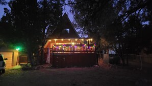 Une maison dotée d’un porche couvert, décoré de guirlandes lumineuses colorées, et entourée d’arbres.