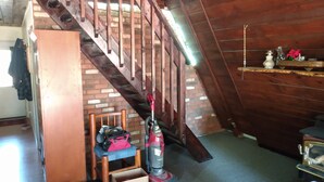Une chambre à coucher aménagée dans un grenier, avec un escalier en bois, une petite chaise en bois, un aspirateur et une boîte étiquetée « Bijou de la couronne ».