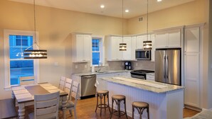 A modern kitchen with white cabinets, stainless steel appliances, and a central island with stools. - Beautiful Newer Construction 5 BR 3.5 bath (Ocean City)