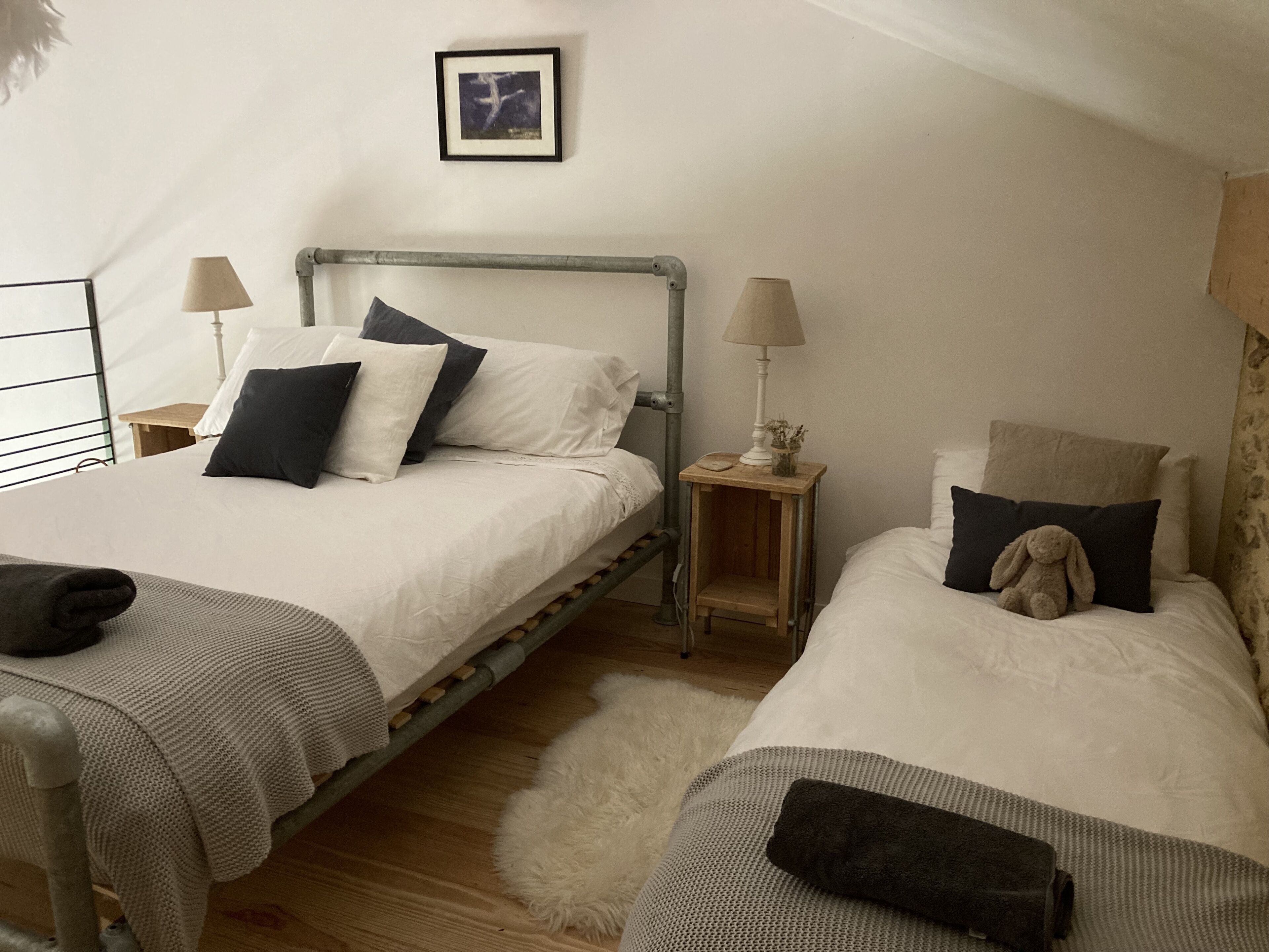 Un dormitorio con dos camas individuales, cada una con una almohada, una mesita de noche con una lámpara y un cuadro enmarcado en la pared.