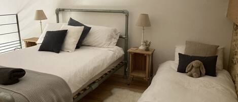 Un dormitorio con dos camas individuales, cada una con una almohada, una mesita de noche con una lámpara y un cuadro enmarcado en la pared.