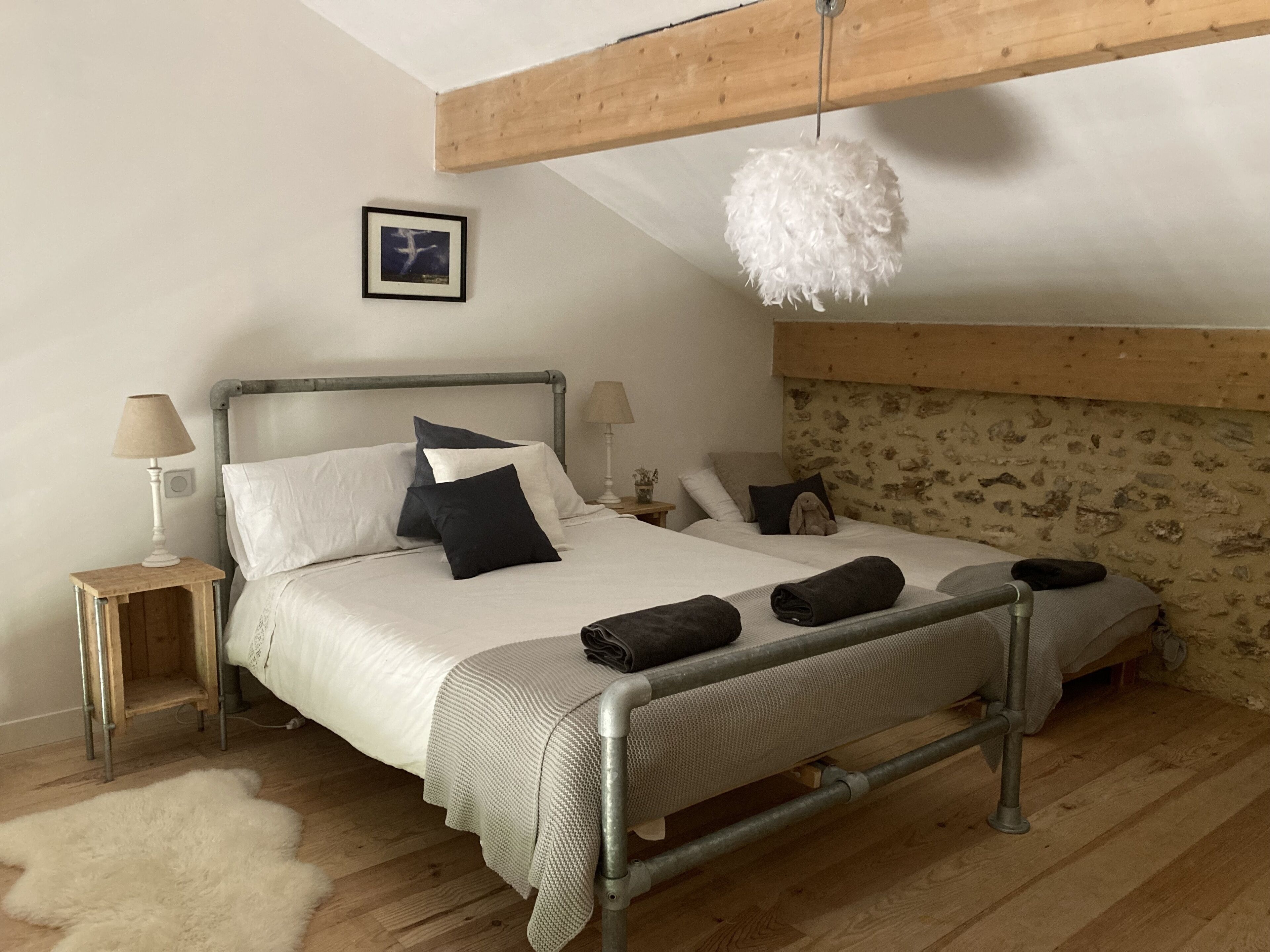 Un dormitorio con una cama, dos mesitas de noche, una lámpara colgante y una pared de piedra.