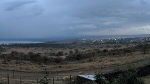 A rural landscape with a dirt road, sparse vegetation, and a distant town with lights. - Beautiful serene home with lake view (Nakuru)