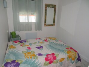 A bedroom with a floral bedspread, a window with curtains, a mirror, and a radiator. - 4 BEDROOM VILLA WITH GREENERY NEAR SANARY PLAGE 20 MN WALK (Six-Fours-les-Plages)