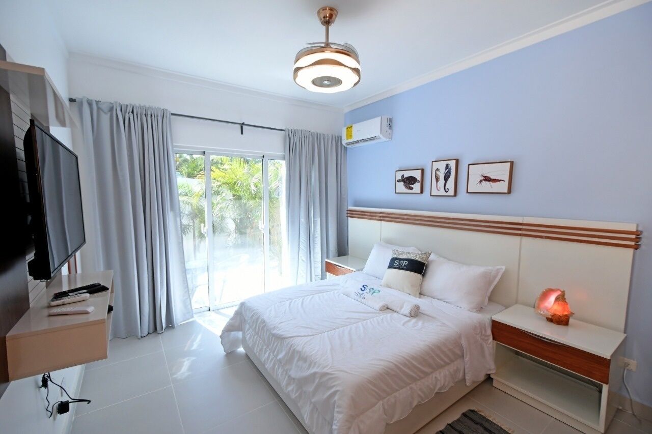 A modern hotel room with a large bed, a TV, a bedside table with a lamp, and a view of the outdoors.