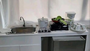 Un angolo cottura compatto con lavandino, macchina del caffè, bollitore e piccolo frigorifero.