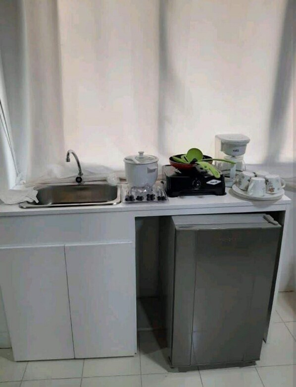 A compact kitchenette with a sink, a coffee maker, a kettle, and a small refrigerator.