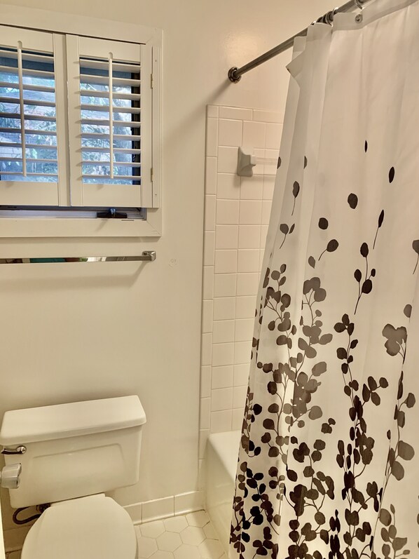 A bathroom with a toilet, a shower with a white curtain, and a window with blinds.