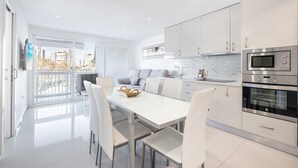 Une cuisine moderne avec des meubles blancs, une table à manger avec des chaises et une grande fenêtre donnant sur la ville.