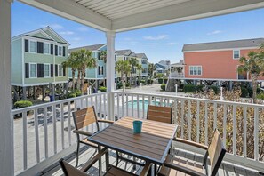 Un espacio de estar techado al aire libre con una mesa y sillas, con vistas a un barrio residencial con casas coloridas y una piscina.