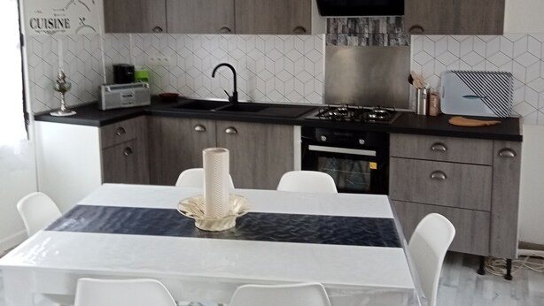 A modern kitchen with grey cabinets, a black range hood, and a dining area with a white table and chairs. - Maison ds Marais Poitevin (Taugon)