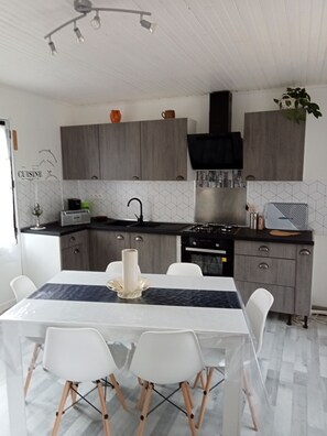 A modern kitchen with grey cabinets, a black range hood, and a dining area with a white table and chairs.