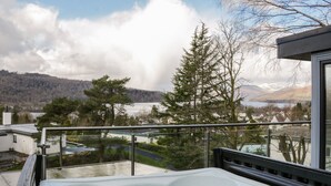 Un jacuzzi en un balcón con vistas a un lago, árboles y montañas al fondo.