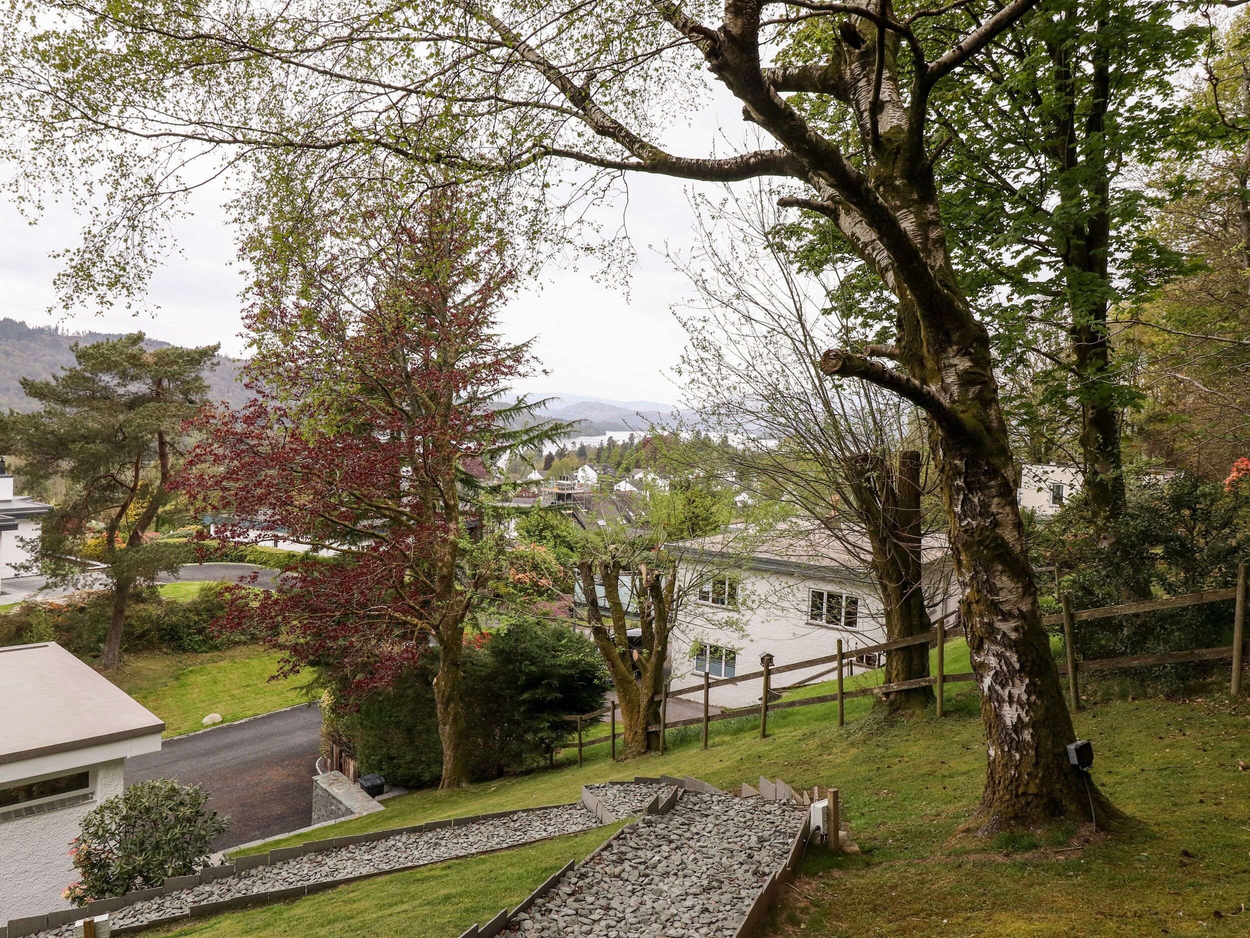 Ett bostadsområde med en asfalterad uppfart, en gångstig av sten och utsikt över hus och en sjö i fjärran.