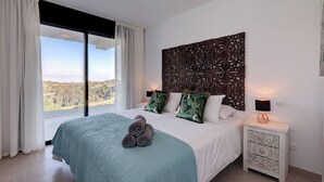 A bedroom with a large bed, a view through a sliding door, a decorative headboard, and a bedside table with a lamp. - Modern 2 Bed Apartment in Trendy La Cala Golf Resort (Mijas)
