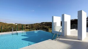 A modern swimming pool with clear blue water, surrounded by white pillars and a view of a hilly landscape. - Modern 2 Bed Apartment in Trendy La Cala Golf Resort (Mijas)