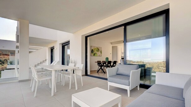 A modern living room with a white sofa, a grey armchair, a white coffee table, and a dining area with a white table and chairs. - Modern 2 Bed Apartment in Trendy La Cala Golf Resort (Mijas)
