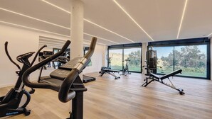 A modern gym with cardio machines, weightlifting equipment, and large windows offering a view of the outdoors. - Modern 2 Bed Apartment in Trendy La Cala Golf Resort (Mijas)