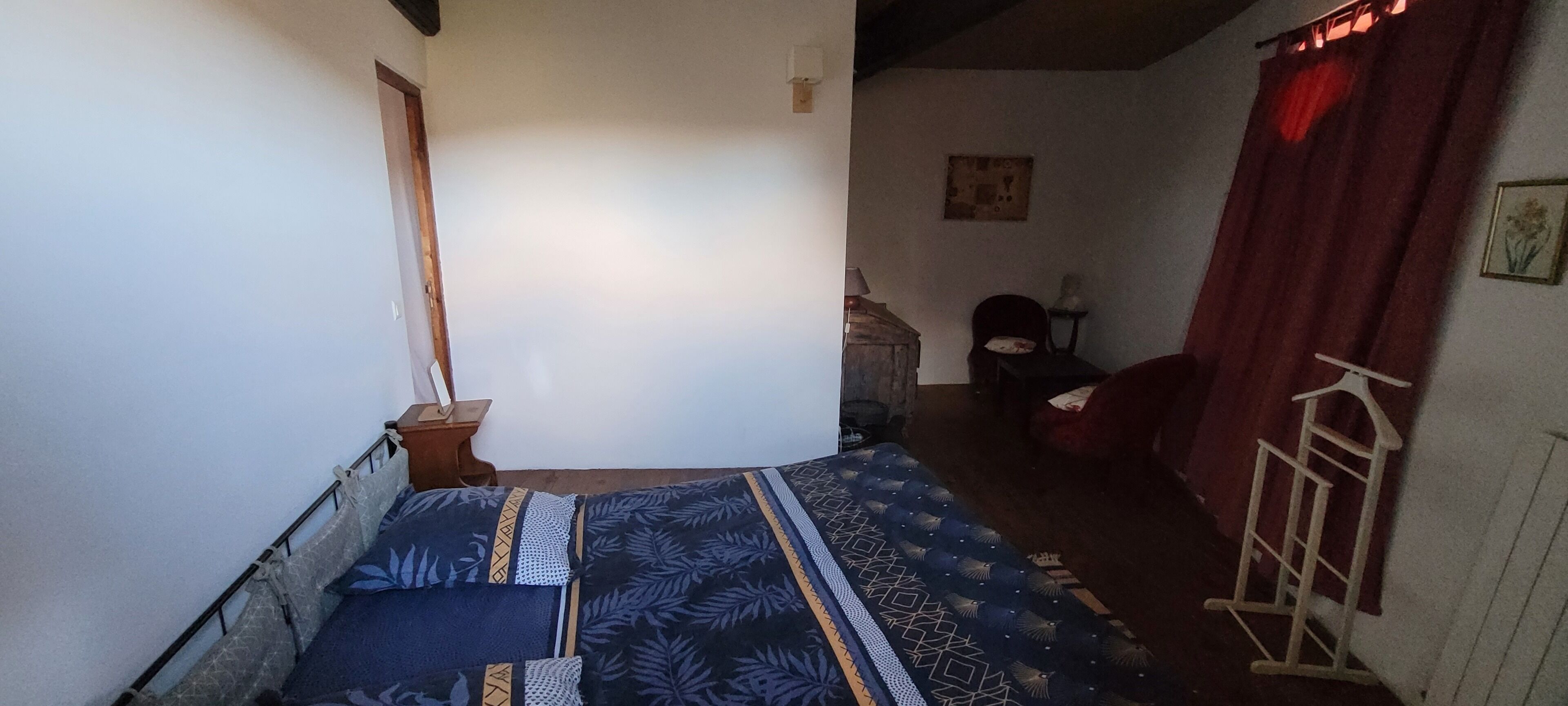 A bedroom with a bed, a nightstand, a chair, and a window with a curtain.
