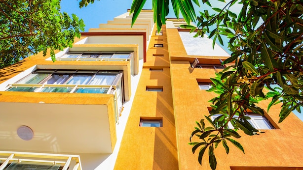 A multi-story building with balconies, large windows, and a tree with green leaves in the foreground. - CherryWood Apartments (Nairobi)
