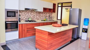 A modern kitchen with wooden cabinetry, a built-in stove, a microwave, and a refrigerator. - CherryWood Apartments (Nairobi)