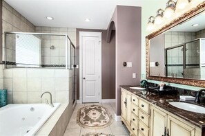 Une salle de bain avec une baignoire, deux lavabos, un grand miroir et une porte.