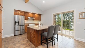 A modern kitchen with a large island, stainless steel appliances, wooden cabinets, and a sliding glass door to the patio. - Cozy cottage home close to nature includes game room, fitness equip, & Hot Tub. (Portland)