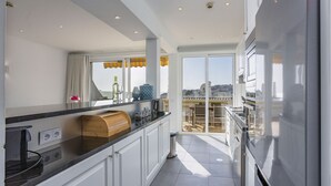 A modern kitchen with white cabinets, a black countertop, and a view of the city through large windows. - Clube do Monaco Stunning Beachfront Apartment Overlooking Town (Albufeira)