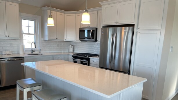 A modern kitchen with white cabinetry, a stainless steel refrigerator, a built-in oven, and a large island with bar stools. - Luxury Newer construction -5BR 3.5 bath  2nd floor (Ocean City)