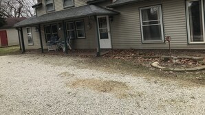 A two-story house with a front porch, a covered patio, and a gravel driveway.