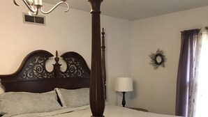A bedroom with a four-poster bed, a chandelier, a wall-mounted heater, a bedside lamp, and a decorative wreath.
