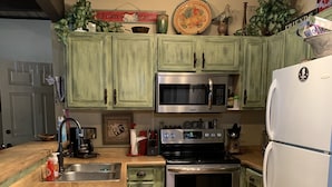 A kitchen with green cabinets, a stainless steel microwave, oven, and refrigerator. There is a wooden countertop, a sink, and various kitchen items. - Sports Village Lower Unit Comfy Mountain Retreat (Pinetop)