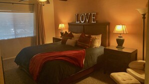 A bedroom with a bed, two bedside tables with lamps, a ceiling fan, a window with blinds, and a wall with the word "LOVE" above the bed. - Sports Village Lower Unit Comfy Mountain Retreat (Pinetop)