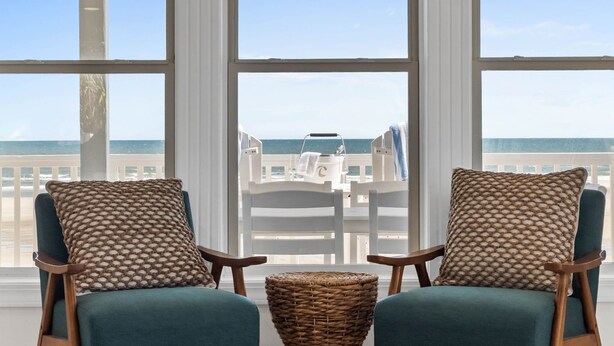 A room with two chairs and a wicker basket, large windows with a view of the beach and ocean. - Fall Available | Oceanfront Home w Panoramic Views (Ocean Isle Beach)