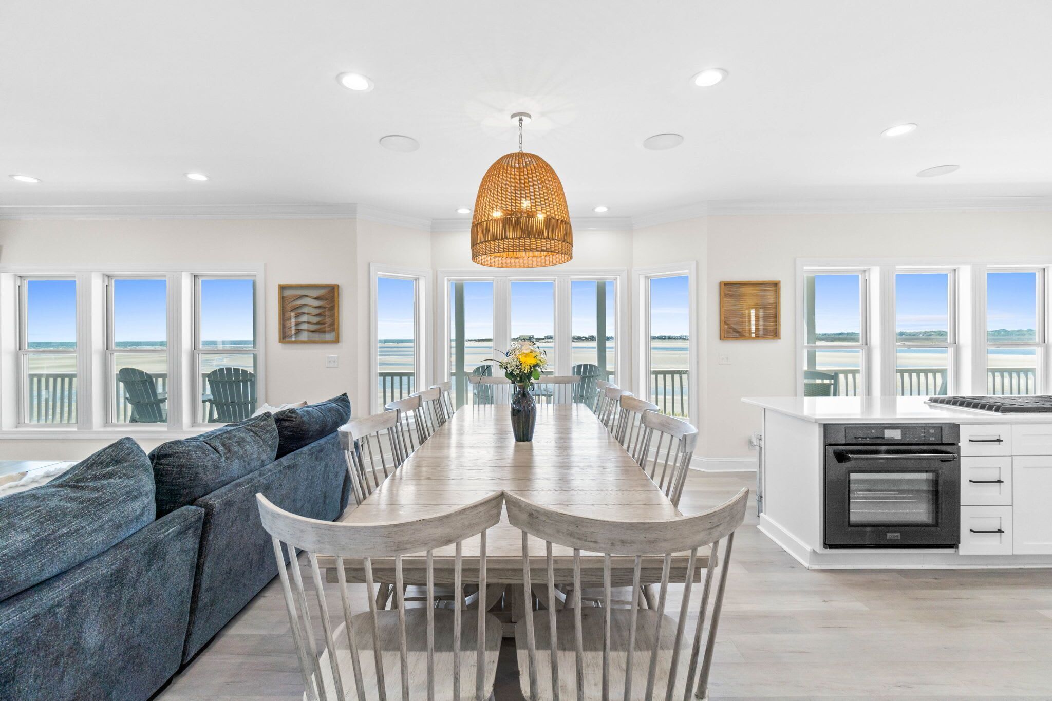 A spacious dining area with a long table, white chairs, and a central vase with flowers.