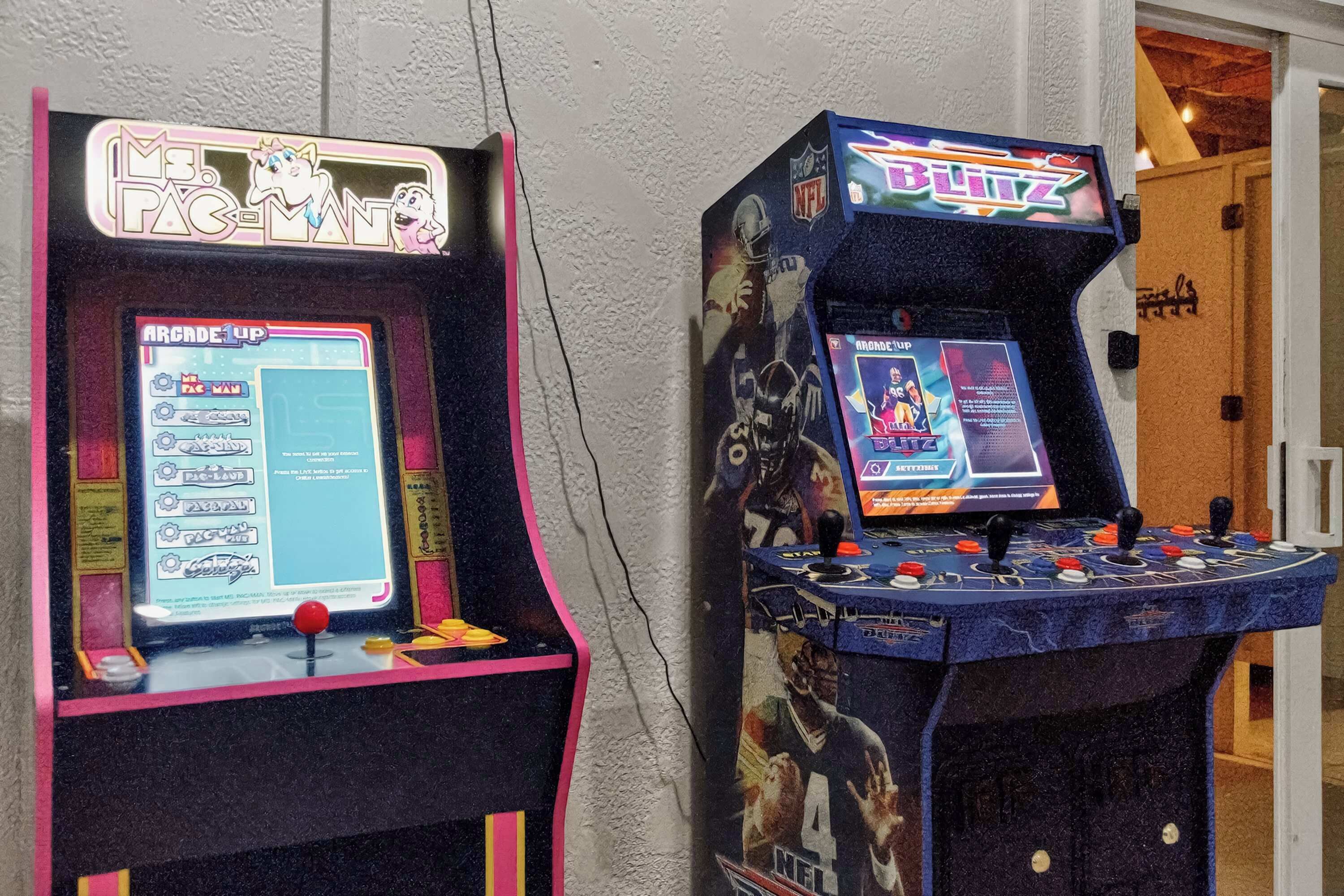 Two arcade machines, one labeled 'PAC-MAN' and the other 'NFL Blitz', against a white wall.