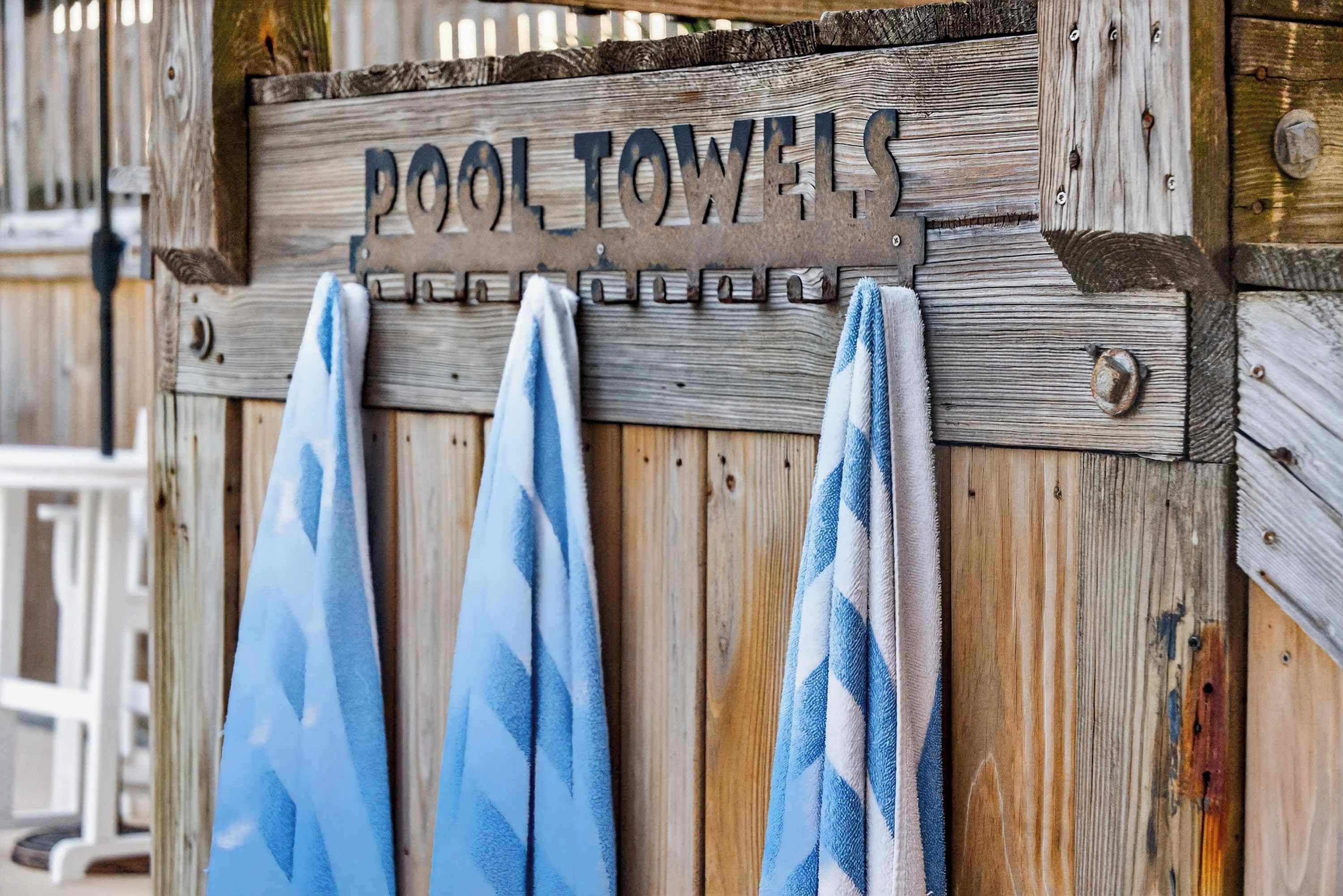 A wooden sign with the text "POOL TOWELS" and three towels hanging below it.
