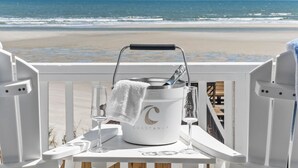 A beachside view with a white bucket labeled "COASTWAY" on a table, two glasses, and a towel. - Fall Available | Oceanfront Home w Panoramic Views (Ocean Isle Beach)