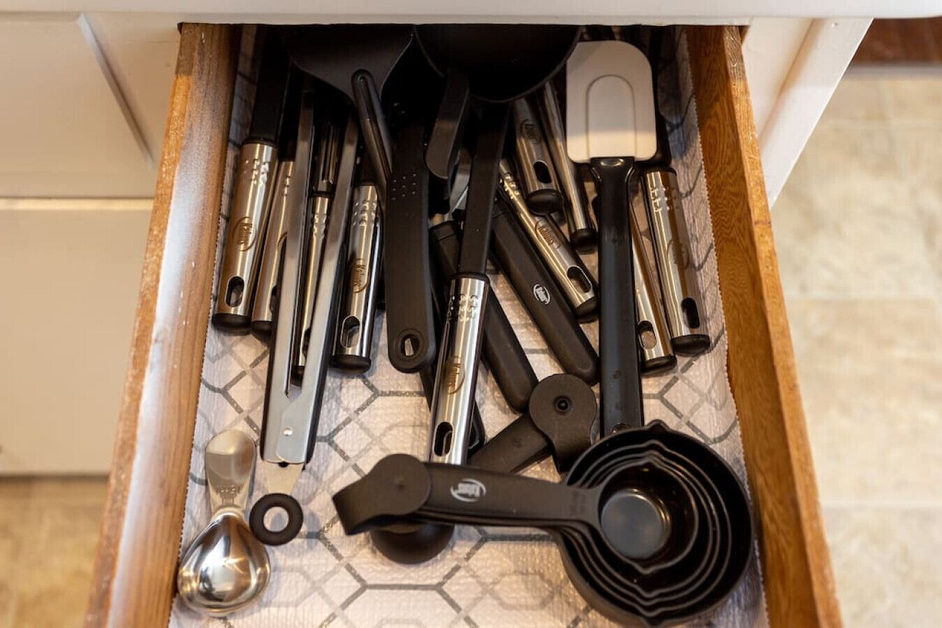 Un cassetto pieno di utensili e strumenti da cucina, tra cui misurini, spatole e una frusta.