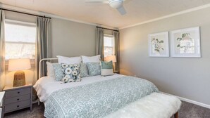 Ein Schlafzimmer mit einem Bett, Nachttischen, einem Deckenventilator und zwei gerahmten Bildern an der Wand.