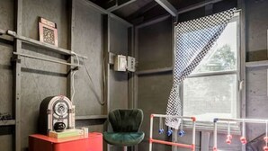 Ein Zimmer mit einem roten Schrank, einem grünen Sessel und einer Metallkonstruktion mit Gewichten.