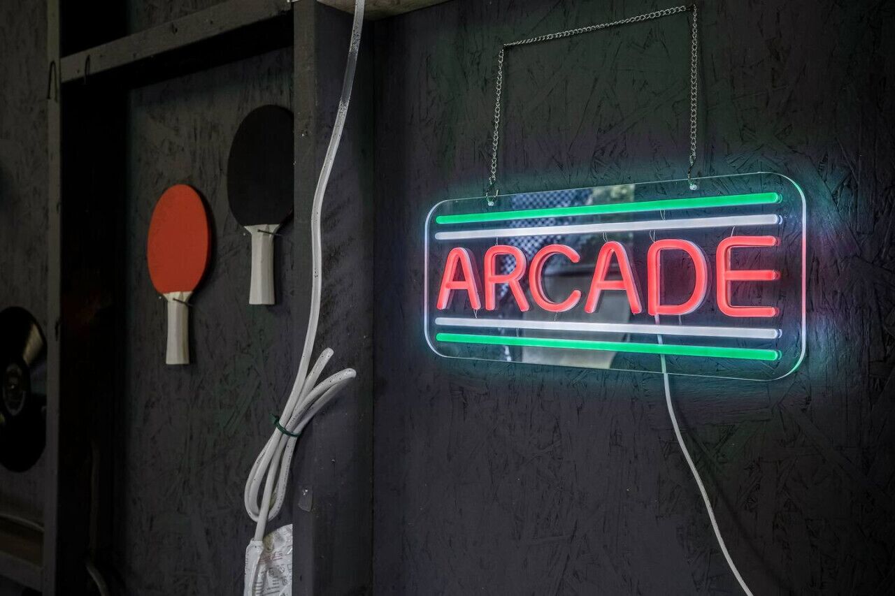 Een neonbord met de tekst 'ARCADE' op een structuurrijke muur, met twee pingpongbats aan de linkerkant.