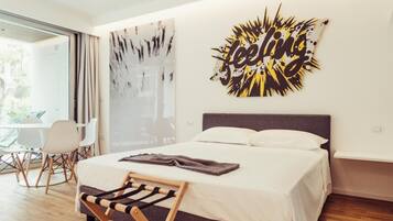 A modern hotel room with a large bed, a view to the outside, and a wall art piece.