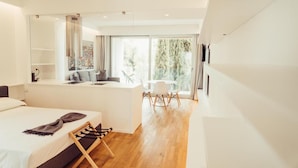 A modern hotel room with a large bed, a desk, and a dining area with a view of the outdoors.